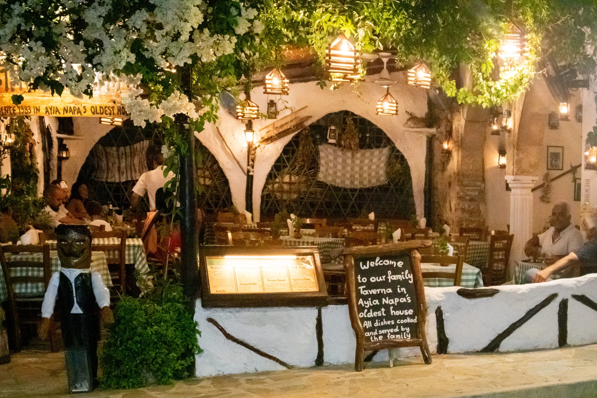 Stamna's stone-arched entrance, green foliage and warmly lit tables at dusk